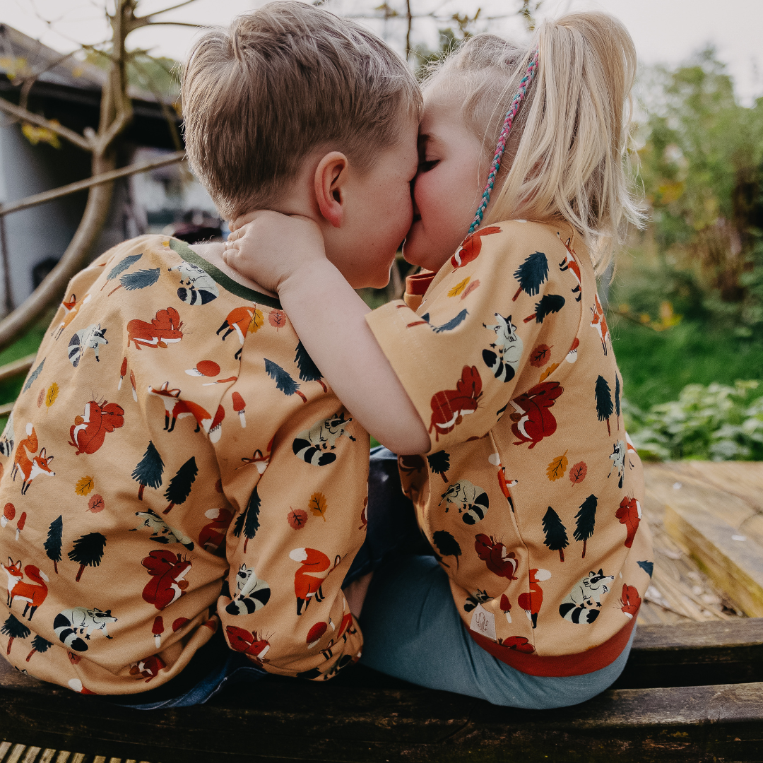 Zwei Kinder sitzen im Garten und tragen das mitwachsende T-Shirt für Kinder im Motiv Waldgewusel von der Marke Oktopulli
