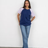 Eine Frau trägt das Raglan Shirt von Oktopulli in der Farbe Blau mit fliederfarbenen Ärmeln und lehnt dabei an einer Wand