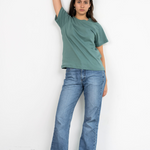 Eine Frau lehnt an einer Wand und trägt ein faires Shirt aus Bio-Baumwolle im Unisex-Schnitt von Oktopulli