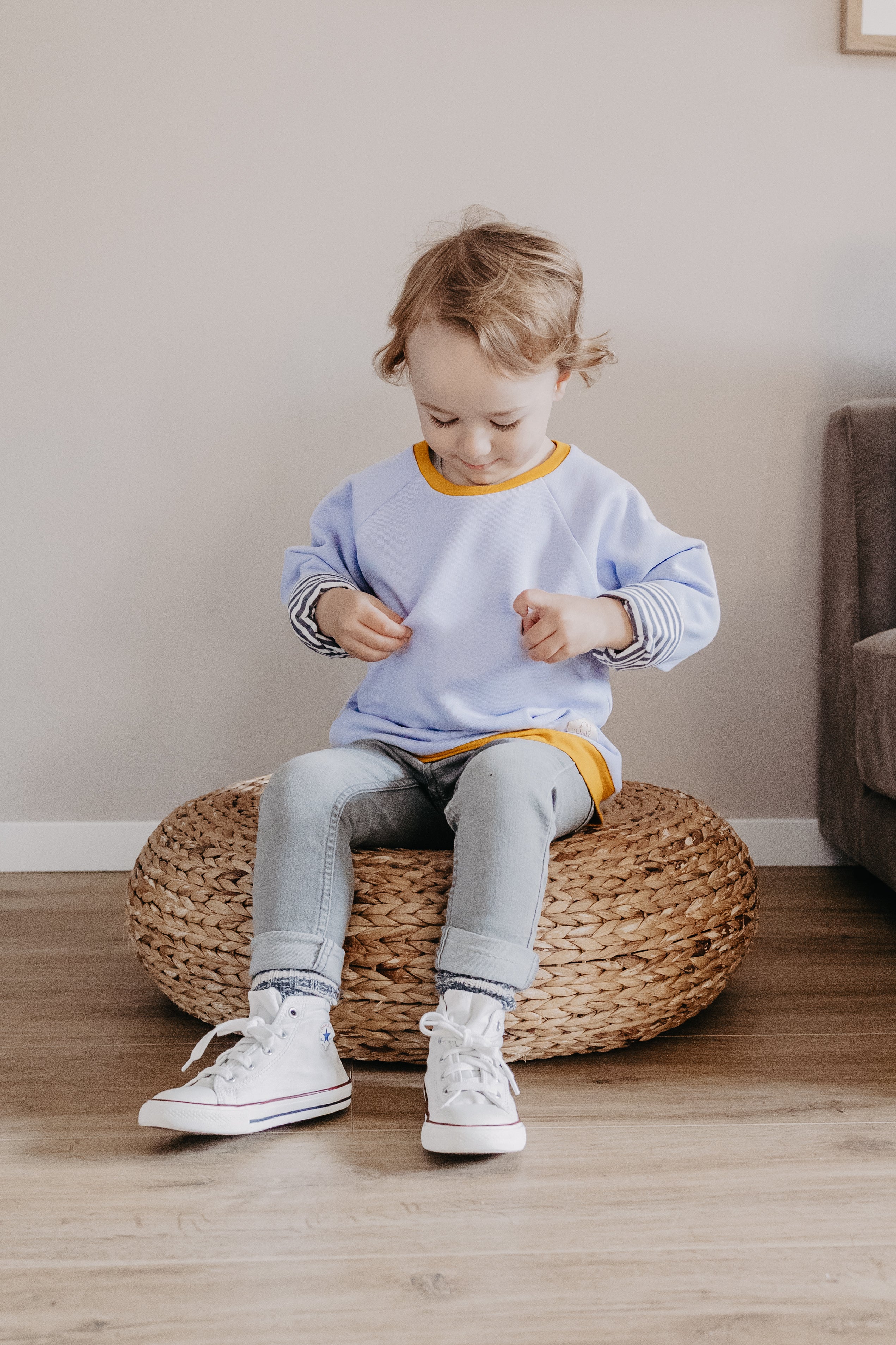 Ein Kind im fliederfarbenen Oktopulli sitzt auf einem geflochtenen Sitzkissen. Kuschelpullover Kinder - für die gemütlichen Stunden 