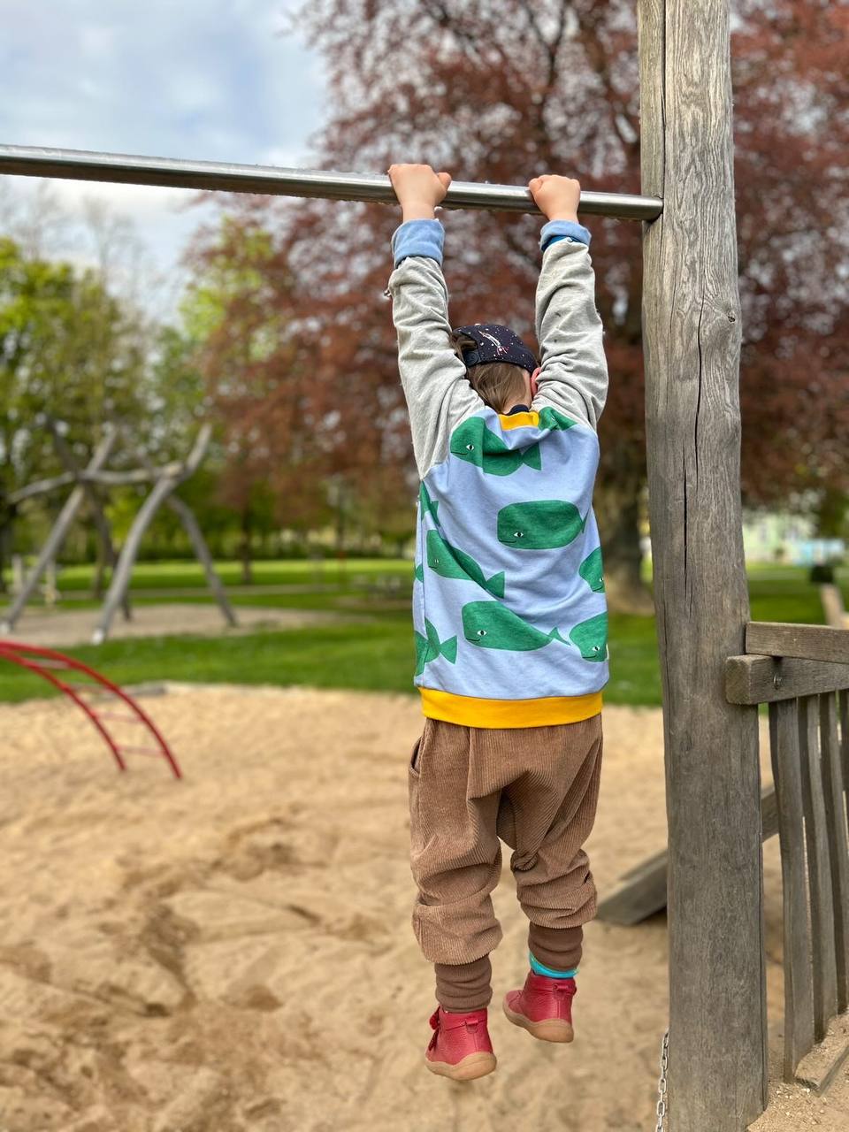 Zweites Bild: Kind auf Spielplatz trägt einen Oktopulli mit aufgedruckten Walen.