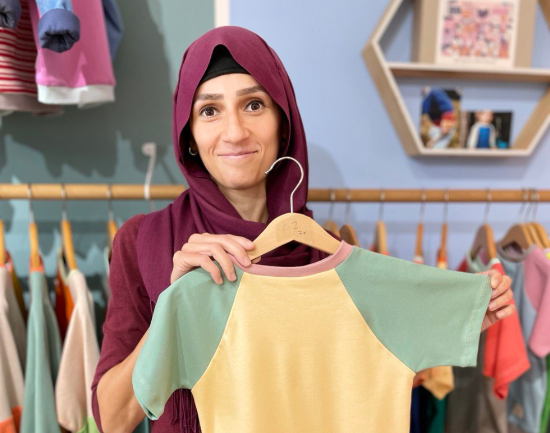 Portrait von der Schneiderin Suzan, die ein Oktopulli T-Shirt in die Kamera hält.