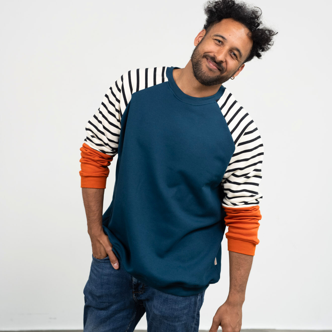 Ein Mann lächelt und trägt den genderneutralen Kuschelpullover  in Blau mit gestreiften Ärmeln von der Marke Oktopulli