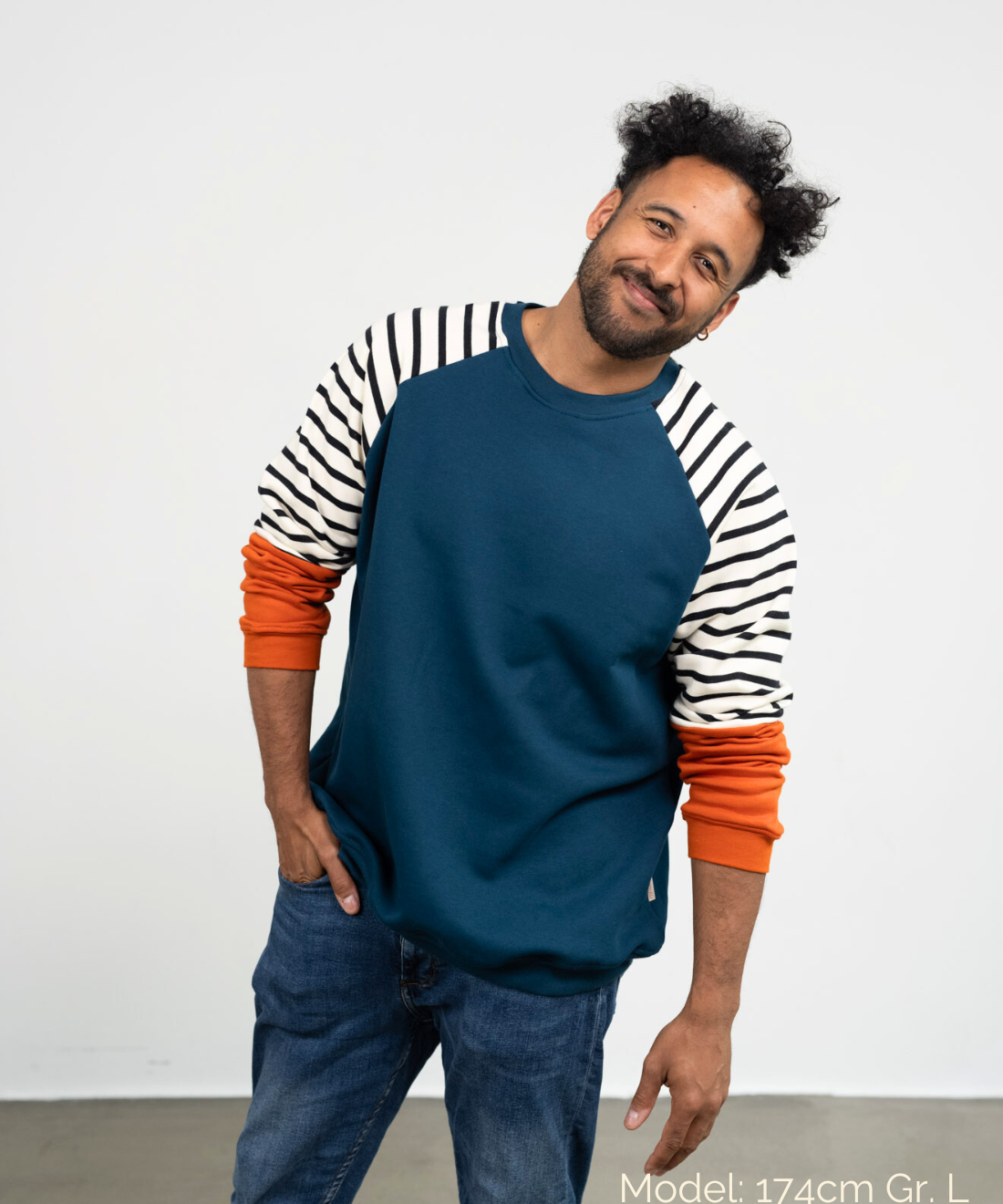 Ein Mann lächelt und trägt den genderneutralen Kuschelpullover  in Blau mit gestreiften Ärmeln von der Marke Oktopulli