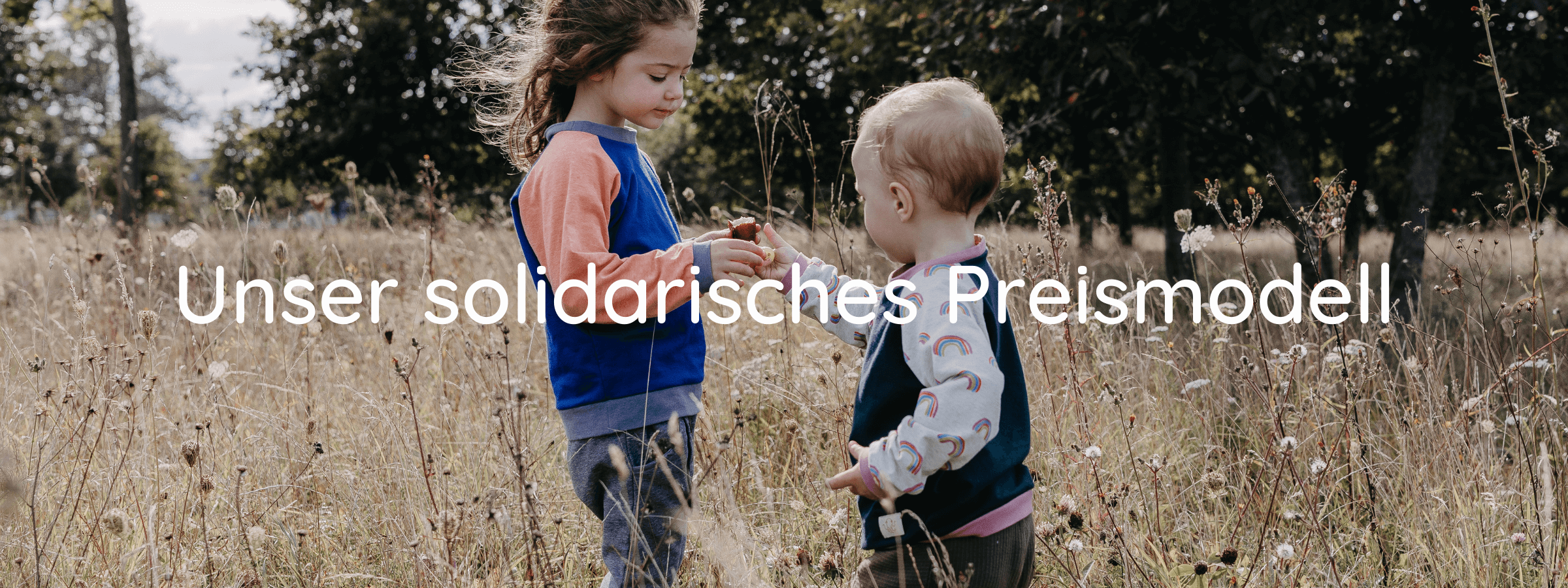 Zwei Kinder stehen auf einer Wiese und reichen sich die Hand. Beide tragen einen Oktopulli. 