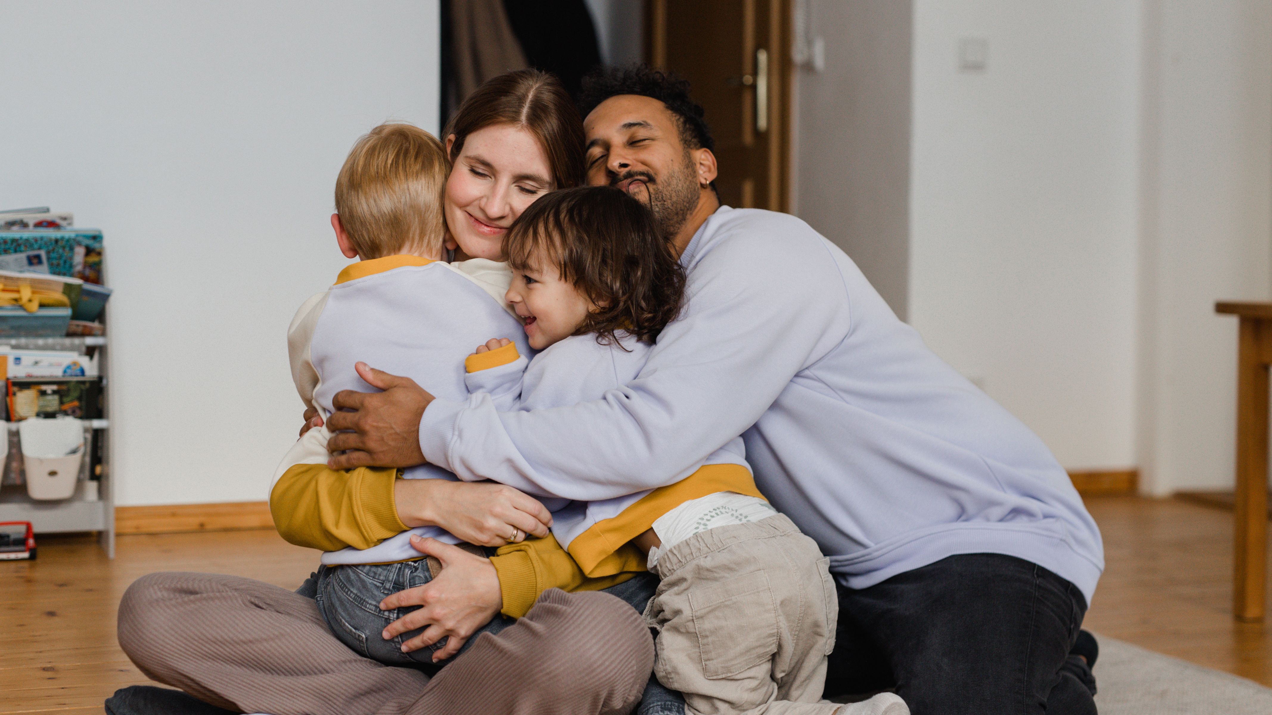 Glückliche Familie in fliederfarbenen Oktopullis in einem Kinderzimmer. Text auf dem Bild: lokal gefertigte Kleidung für Klein und Groß. Für Kinder