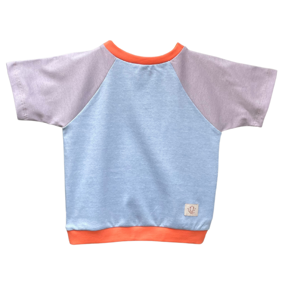 Raglan Kinder T-Shirt. Korpus hellblau meliert. Ärmel lila meliert. Bündchen an Hals und Saum orangerot. 