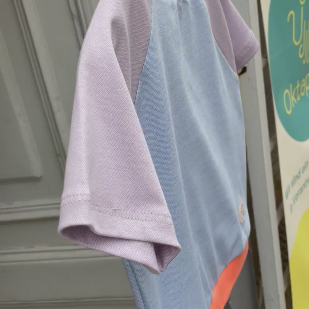 Raglan Kinder T-Shirt. Korpus hellblau meliert. Ärmel lila meliert. Bündchen an Hals und Saum orangerot. 