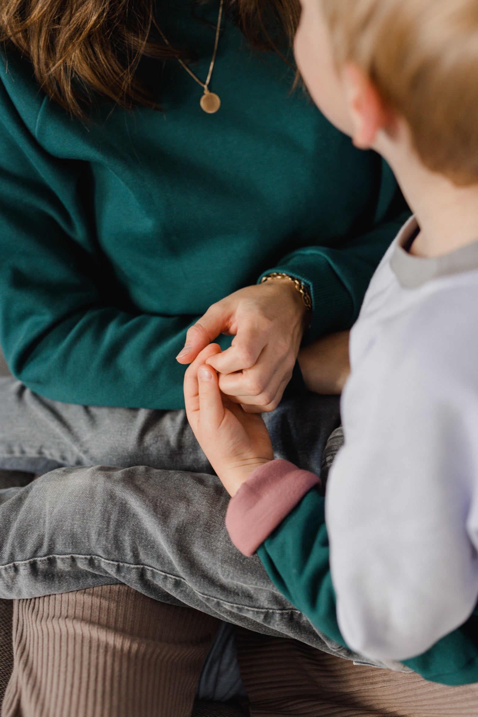 Nahaufnahme von einem Kind im grünen und fliederfarbenen Oktopulli sitzt auf dem Schoß seiner Mutter, die einen smaragdgrünen Oktopulli trägt. 