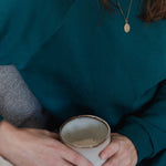 Nahaufnahme von Frau im smaragdgrünen Oktopulli. In ihren Händen hält sie eine Tasse.