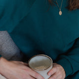 Nahaufnahme von Frau im smaragdgrünen Oktopulli. In ihren Händen hält sie eine Tasse.